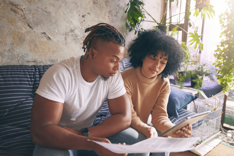 Shot of a young couple using a digital tablet while going through paperwork together at home.