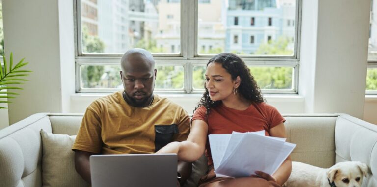A young interracial couple working on their budget and finances on a sofa from home with their dog using a laptop computer, stock photo