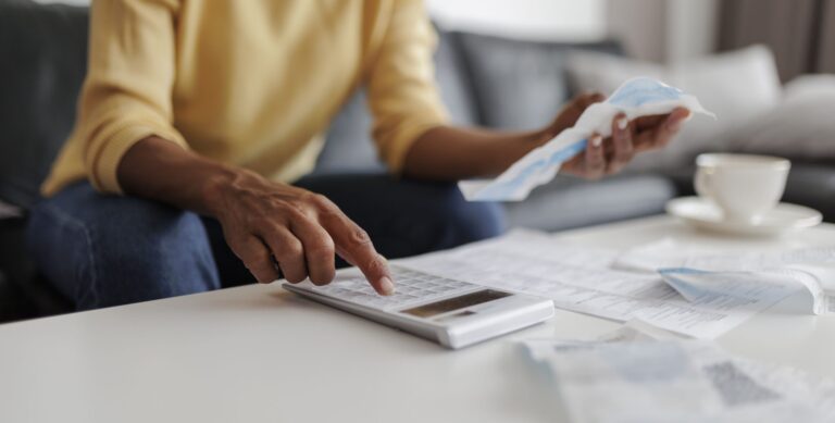 Close up of a mid adult woman calculating her bills at home, sitting in her living room.