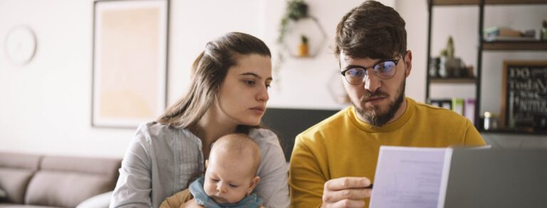 Young family with baby sitting at kitchen table with bills and laptop reviewing finances