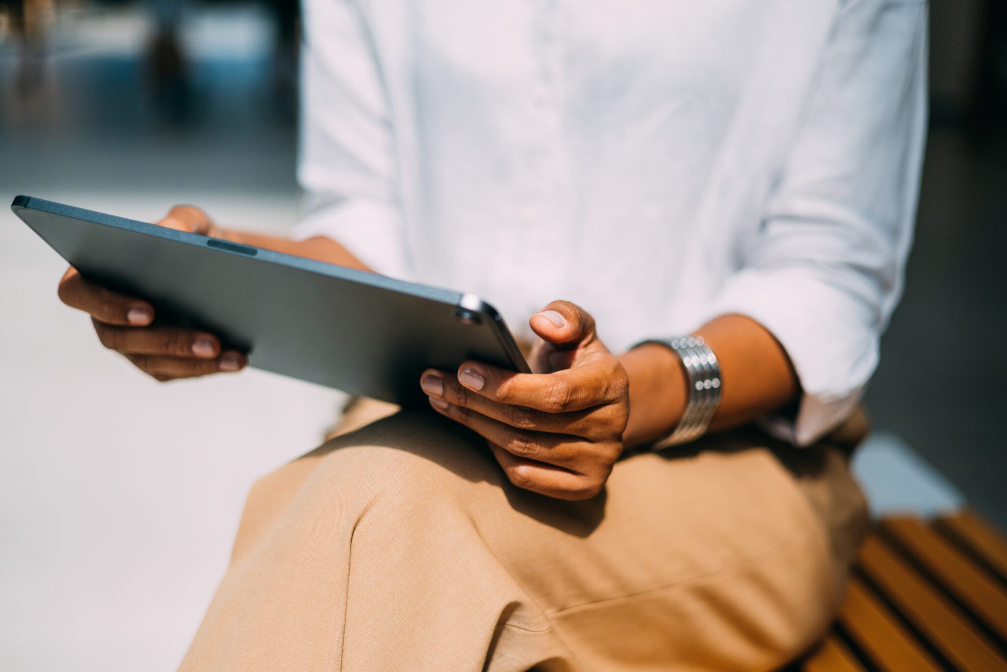 A woman's hands holding a tablet on bench