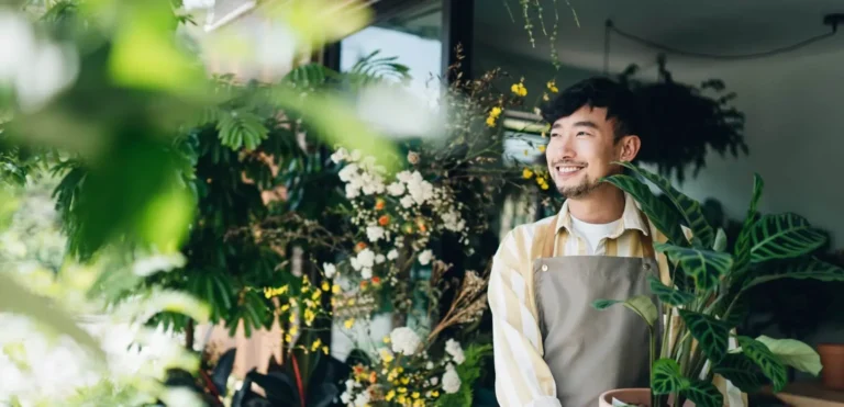 Male plant shop employee smiling and holding a potted plant.