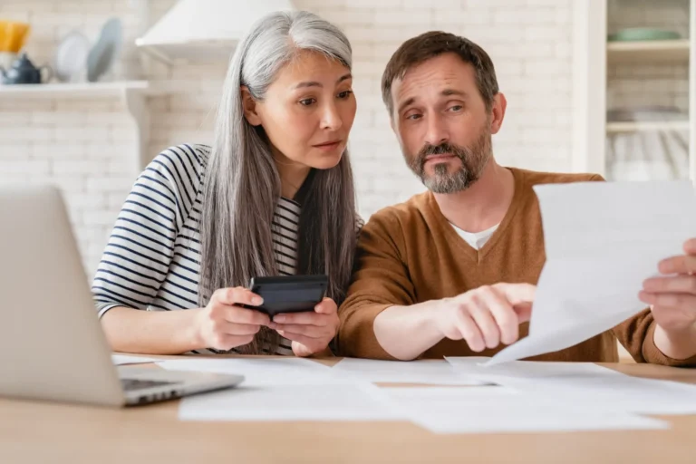 Mature middle-aged couple wife and husband doing paperwork with calculator and laptop