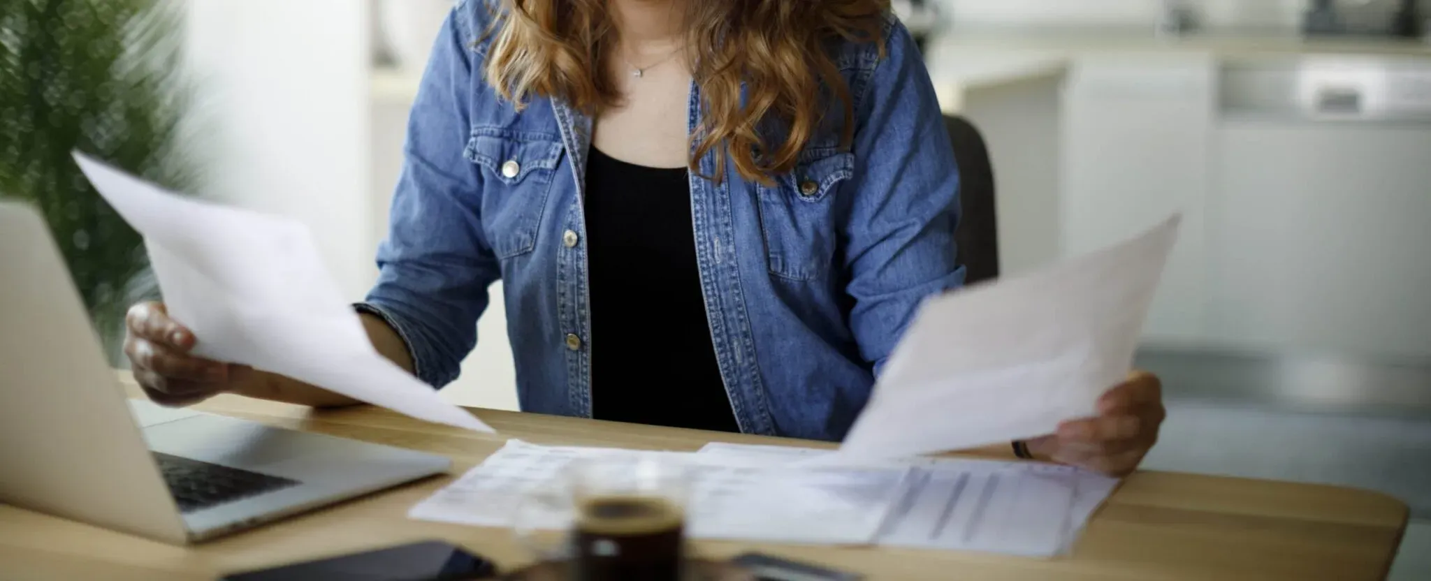 Serious young woman reviewing papers in front of her laptop at home