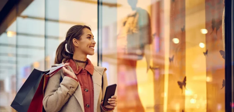 Happy woman with shopping bags looking at store windows while walking through the mall