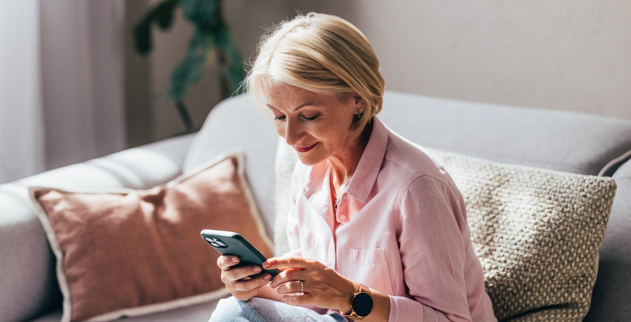 A happy mature woman sitting on her couch looking at her phone