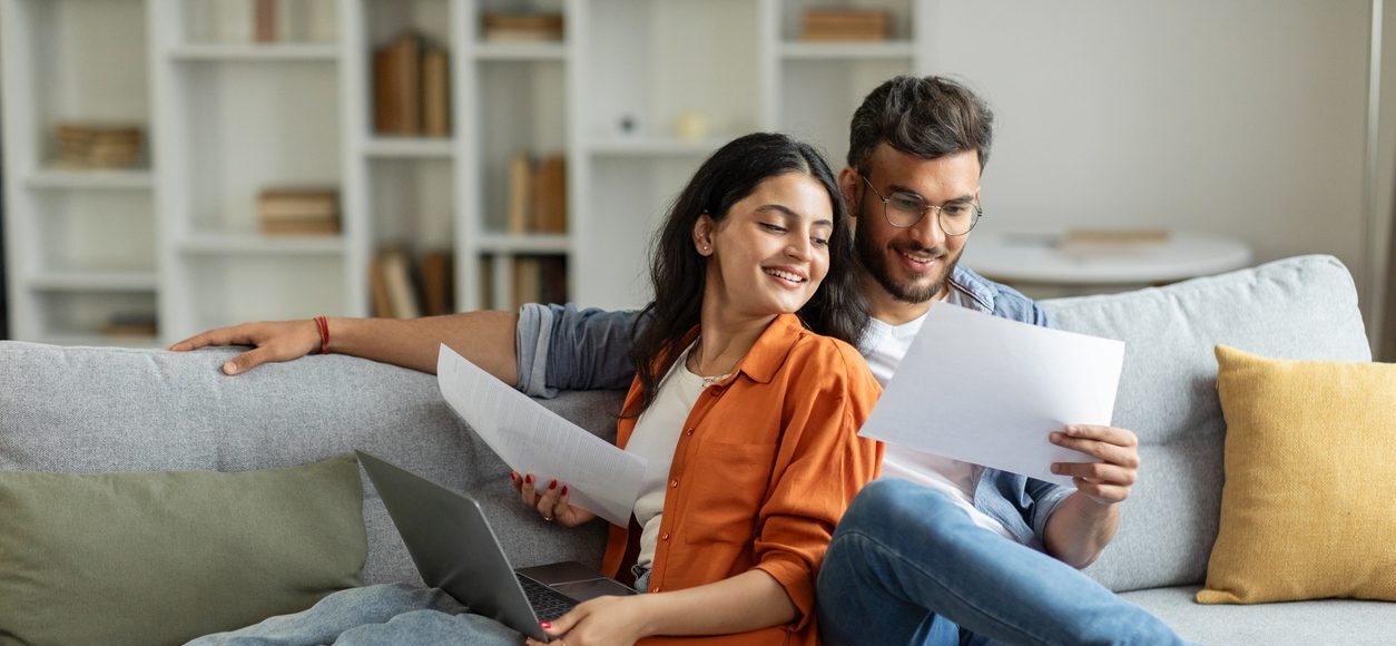 Happy young couple sitting on couch looking at documents together