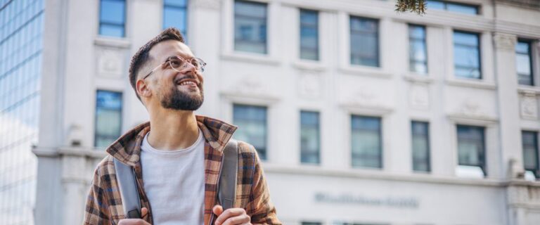 Smiling young male walking in city streets with a backpack
