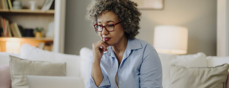 Mature woman sitting on couch looking at laptop looking contemplative yet content