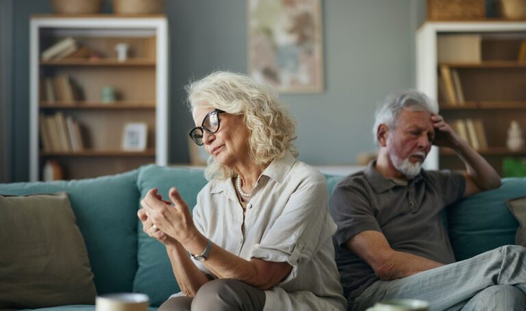 Senior couple sitting on couch looking disappointed with each other