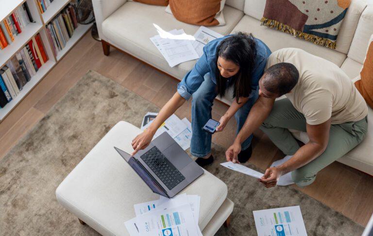 High angle view of a couple at home paying bills online using a laptop with financial documents around them